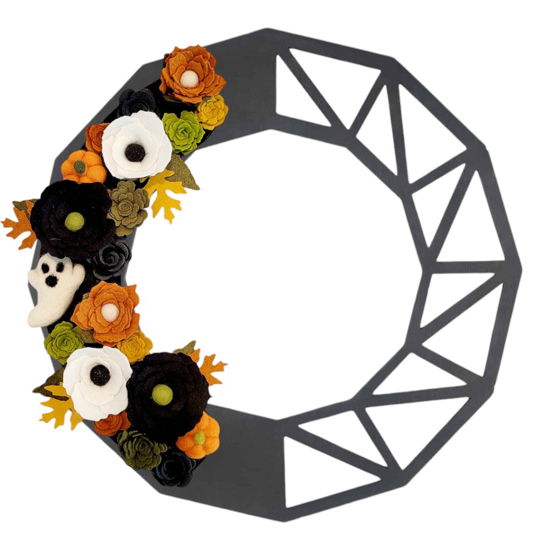 An interchangeable Halloween wreath made from sustainable materials, featuring vibrant felt flowers in orange, green, black, and white on a black geometric wreath base.