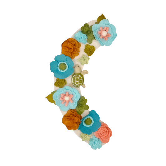 With vibrant teal, green, brown felt flowers and felted sea turtle are evoking a coastal vibe and symbolizing ocean habitats.