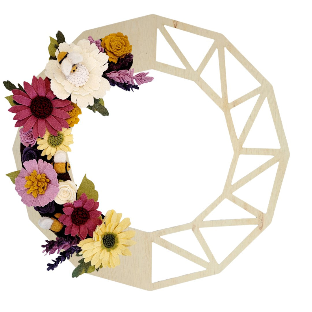 This charming wreath promotes the "Save the Bees" movement, featuring delightful felt bees buzzing among vibrant purple and yellow flowers on a birch geometric base.