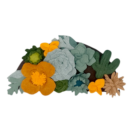 A felt arrangement of various succulents and flowers, including cacti, in shades of green, yellow, and brown on a dark background.