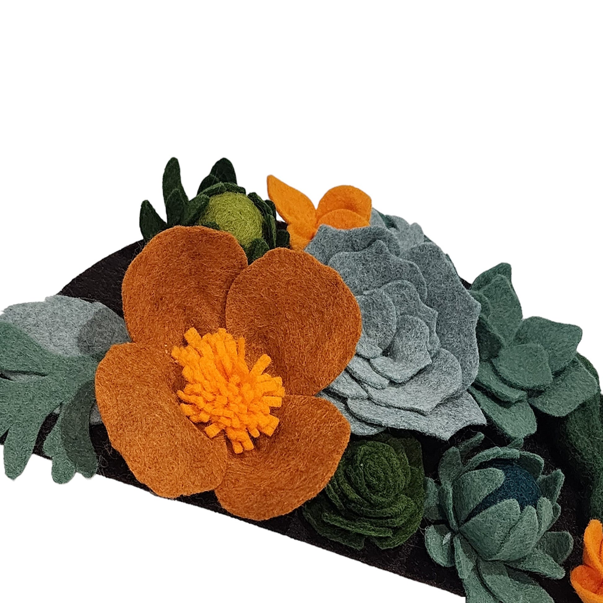 Close up of a felt arrangement of various succulents and flowers, including cacti, in shades of green, yellow, and brown on a dark background.